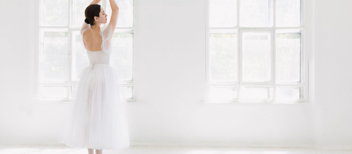 Young and incredibly beautiful ballerina is posing and dancing in a white studio full of light.